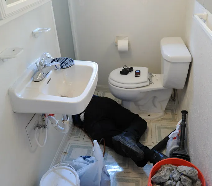 A technician working on an exposed drain line beneath a bathroom fixture